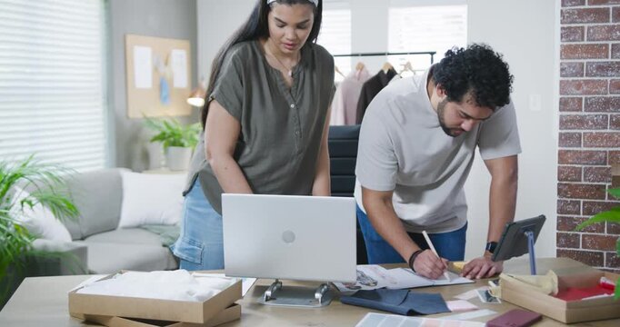African American partners man writing notes, woman checking laptop and swatches, ordering in studio