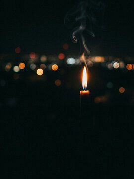 Close-up of a single lit candle flame against a dark background with soft bokeh lights