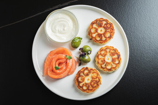 Savory Syrniki with Smoked Salmon, Olives and Sour Cream on White Plate
