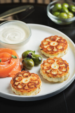 Savory Syrniki with Smoked Salmon, Olives and Sour Cream on White Plate