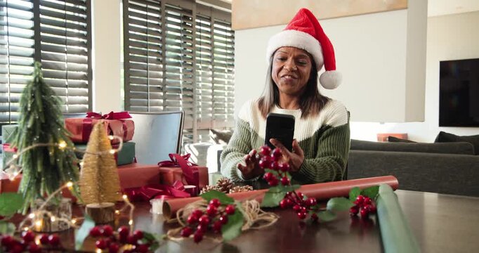 Senior African American woman answering phone call at table with gifts, gesturing for holiday chat