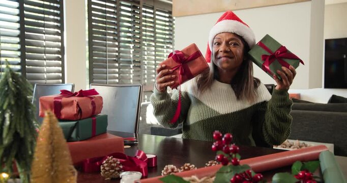 Mature African American woman in Santa hat finishing wrapping and comparing boxes at dining table