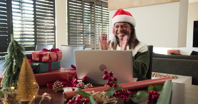 Mature African American woman sitting at table in Santa hat, joining holiday laptop call, clapping