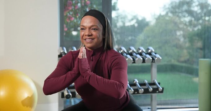 African American woman after cue, rising to standing and extending arms at home gym with dumbbells