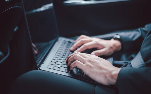 Close up of a businessman hands typing on a laptop keyboard inside a luxury car, working remotely during business travel or commuting, reflecting mobile office lifestyle and digital connectivity