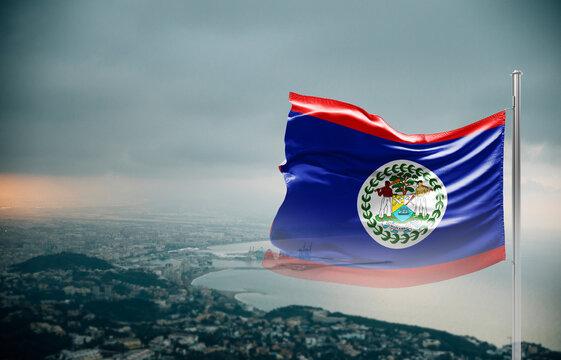 Belize flag waving over a coastal city under dramatic cloudy sky, realistic fabric motion, aerial seaside landscape background. Belize national flag for independence day.