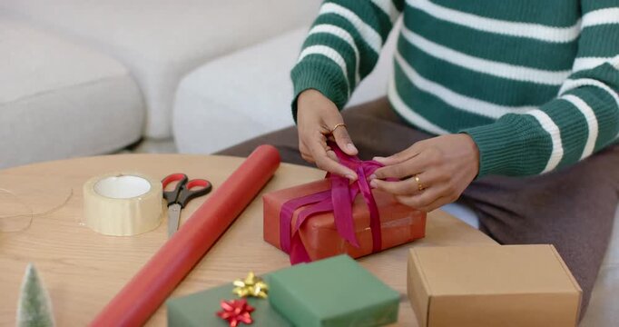 Hands are laying magenta ribbon across wrapped red box, tying bow on wooden table for gift