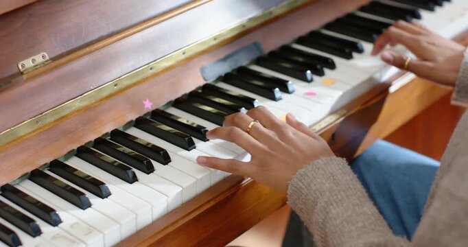 Hands coming and landing on mid lower piano keys near window, pressing stickers and practicing