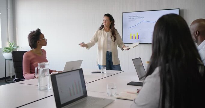 Diverse team watching beige presenter presenting at meeting table, rising chart sparking high-five
