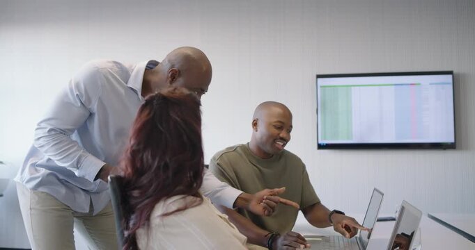 Diverse team in office, mature man placing hand on chest, pointing at laptop, aligning data