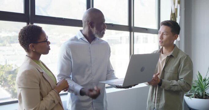 Diverse team at office, Asian man holding laptop reviewing, African woman pointing, man moving it