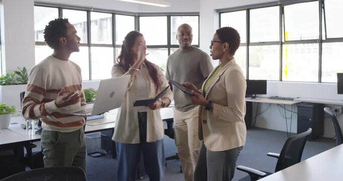 Diverse coworkers holding binder and tablet showing laptop in open office two joining sharing notes