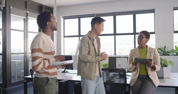 Diverse team standing by windows left man holding laptop showing update right woman tapping tablet