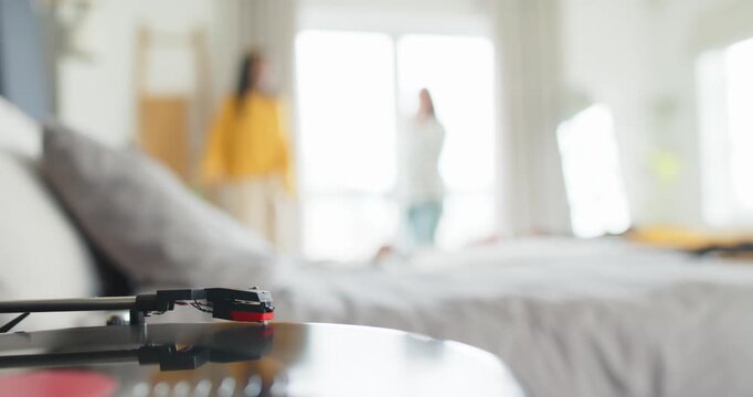 Record player tonearm is remaining still while two friends are entering frame to chat by window