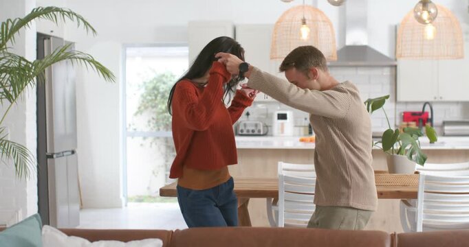 Couple reaching as man taking woman's hand, stepping pivoting in home kitchen playfully connecting