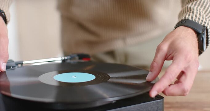 Hands are placing black vinyl with blue label on tabletop turntable lowering tonearm to play