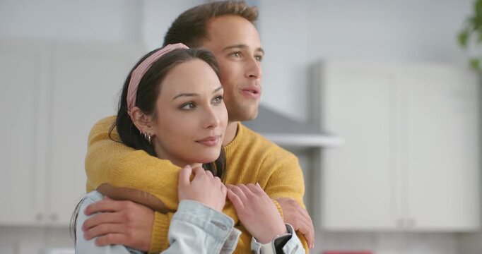 Couple in kitchen, man approaching, embracing woman in denim jacket, pointing toward red toaster