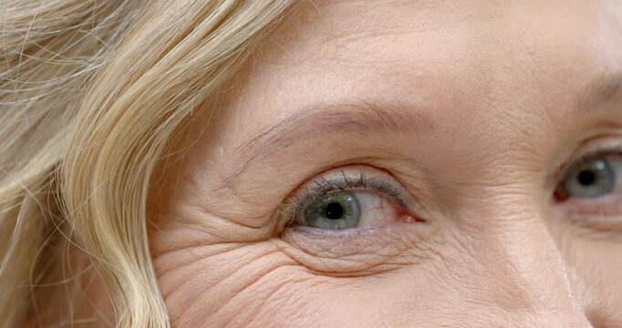 Senior woman's eye is blinking, narrowing, relaxing in studio from camera focus