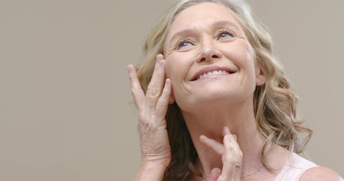 Mature woman looking upward smiling running fingers along jawline posing for beauty shoot in studio