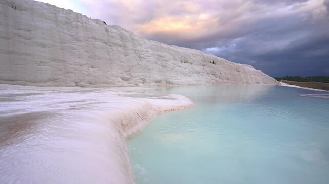 View of Pamukkale travertine terraces with turquoise mineral pools and white limestone formations under a cloudy sky in Pamukkale, Denizli, Turkiye.