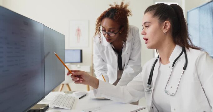Doctors physicians teamwork consultation diagnosis computer records. Two doctors review charts on a clinic monitor and update care. Clear collaborative healthcare clinic analysis concept.