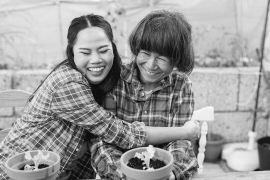 Happy asian mother and daughter having fun together while planting organic lettuce at house terrace - Family people, bonding and lifestyle concept - Black and white editing