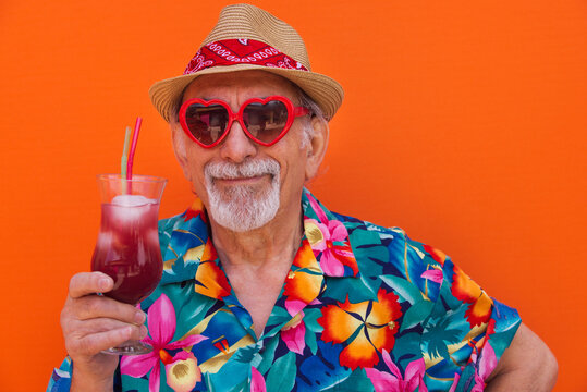 Eccentric senior man portrait wearing hawaiian shirt and drinking tropical cocktail on summer party