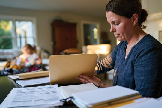A woman carefully examines documents in a cozy home workspace, signifying diligence and commitment to her tasks amidst a warm and inviting atmosphere.