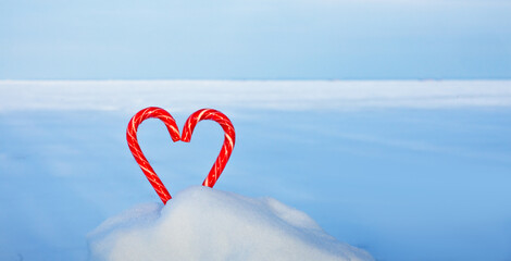 Fototapeta premium Two heart-shaped candy canes are stuck in the snow. The concept of love and Valentine's day, Christmas holiday background, winter season greeting card
