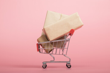 Mini shopping cart with wrapped parcels on pink background © PhamHong