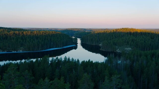 View of Repovesi National Park lake surrounded by dense coniferous forest at sunset in Kouvola, Finland. Panning timelapse.