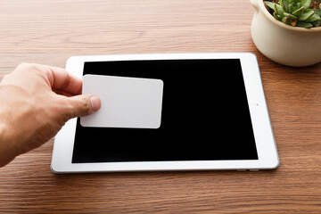 Hand Holding Blank Card Over Tablet on Wooden Desk © PhamHong