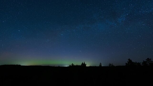 View of Repovesi National Park under the starry night sky with faint aurora borealis above the silhouetted forest in Kouvola, Finland. Timelapse.