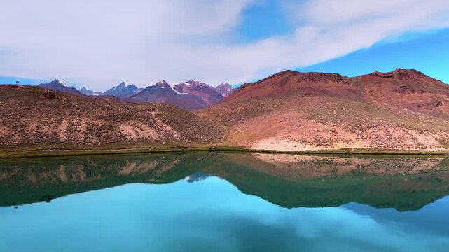 Scenic Cinematic Drone View of Chandratal Lake Near Spiti Valley, Himachal Pradesh Featuring Brilliant Blue Water, Majestic Rocky Mountains and a Clear Sunny Himalayan Landscape