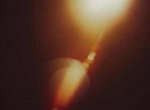 Warm lens flare and light leak background with soft bokeh glow and dark brown tones, cinematic abstract texture for photography, posters, overlays and digital design.