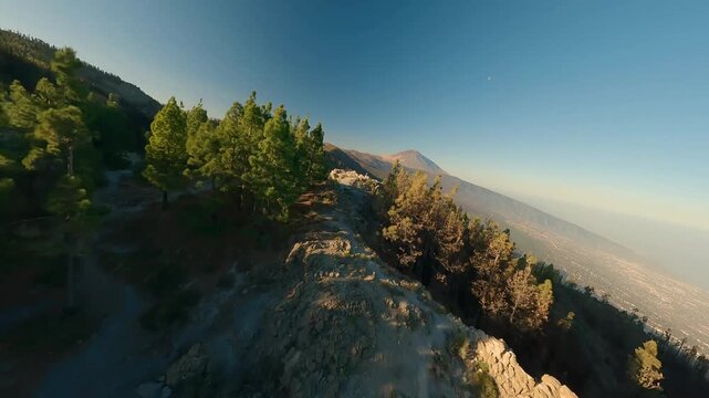 FPV aerial view of a winding mountain road with Mount Teide in the background, surrounded by pine forests and volcanic terrain in Santa Cruz de Tenerife, Canary Islands, Spain.