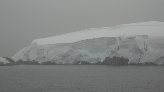 Massive glacier and towering ice cliff rising directly from the sea in the Melchior Islands, Antarctica, viewed in overcast and misty conditions from a cruise ship