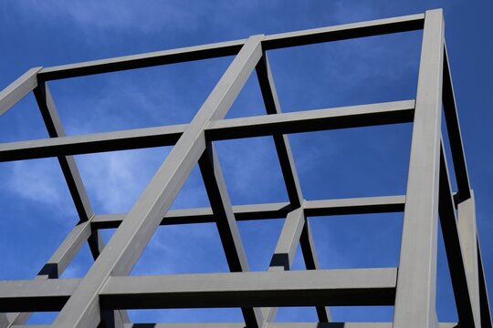 Vue en perspective d'une ossature m&eacute;tallique compos&eacute;e de poutres en acier formant des angles droits et formes carr&eacute;es. Ciel bleu en arri&egrave;re plan. Symbole de solidit&eacute;.