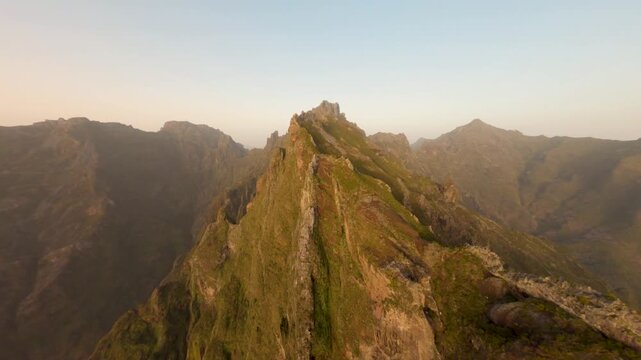 FPV aerial view of sharp mountain ridge at golden hour with rugged cliffs and green slopes in Madeira, Portugal.
