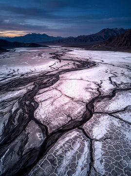 Aerial view of cracked salt pan patterns and meandering water channels at twilight in a desert mountain valley