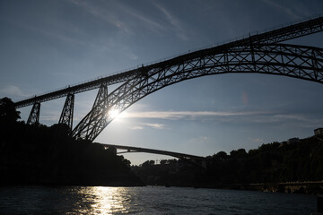 Fototapeta premium The silhouette of the Dom Luís I Bridge in Porto at sunset, with the sun’s rays streaming in from behind.