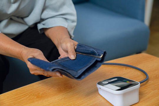 Elderly woman holding measuring her blood pressure with a digital monitor, personal wellness, health monitoring.