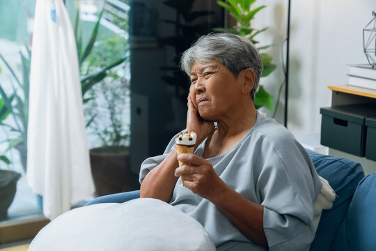 Elderly Asian woman touching her cheek after experiencing tooth sensitivity from eating ice cream, dental discomfort and oral health.