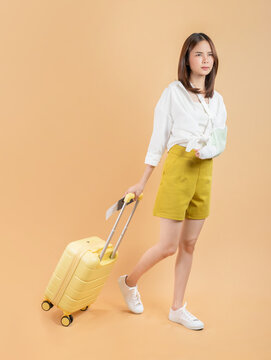 Young Asian woman broken arm wrapped and walking with suitcase on orange background, travel insurance concept.