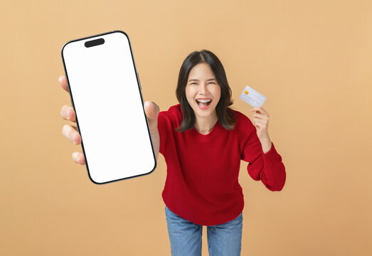 Cheerful Asian woman holding a smartphone with a blank screen and credit card while smiling, online shopping and modern lifestyle concept.