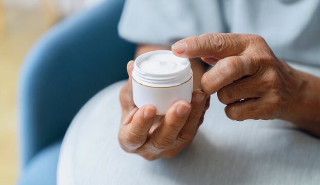 Close-up of an elderly woman wrinkled hand holding a jar of moisturizing cream, skincare and senior beauty.
