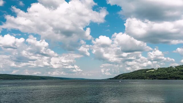 View of a vast lake surrounded by rolling hills under a bright sky filled with fluffy white clouds in the United States.