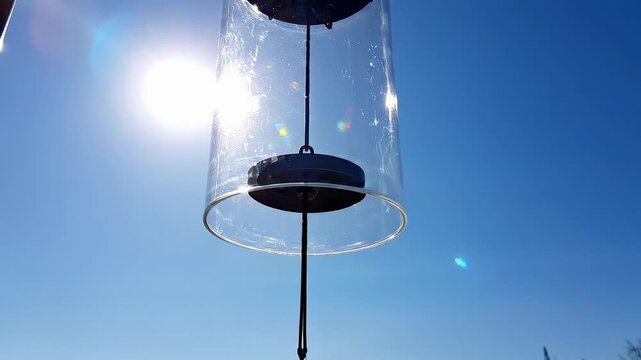 Clear Glass Wind Chime Rotating Against Bright Blue Sky
