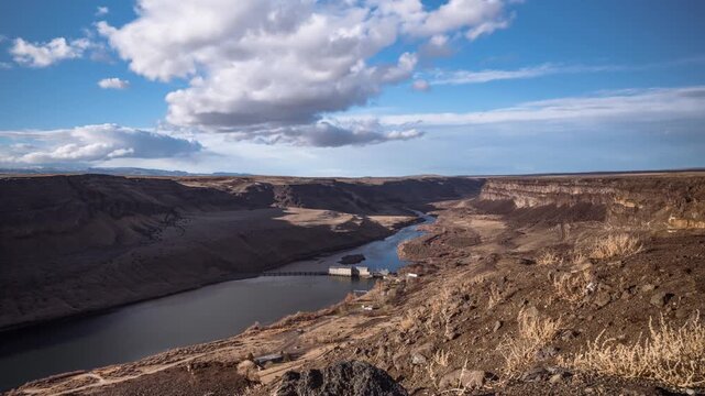 View of the Snake River flowing through a deep, arid canyon with rocky cliffs and a small dam structure under a blue sky in Boise, Idaho, United States.