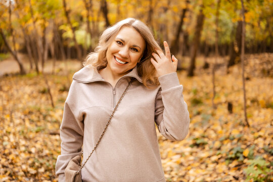 Happy woman in autumn forest smiling at camera &mdash; peaceful weekend recreation. Mental wellbeing concept. Joyful lady resting outdoor enjoying nature connection during beautiful sunny fall day.